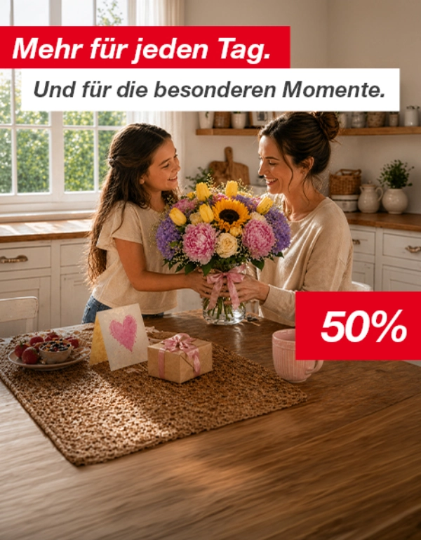 Eine Frau und ein Mädchen sitzen an einem Küchentisch mit einem Blumenstrauß, einer Geschenkbox, einer Grußkarte und einem Becher.