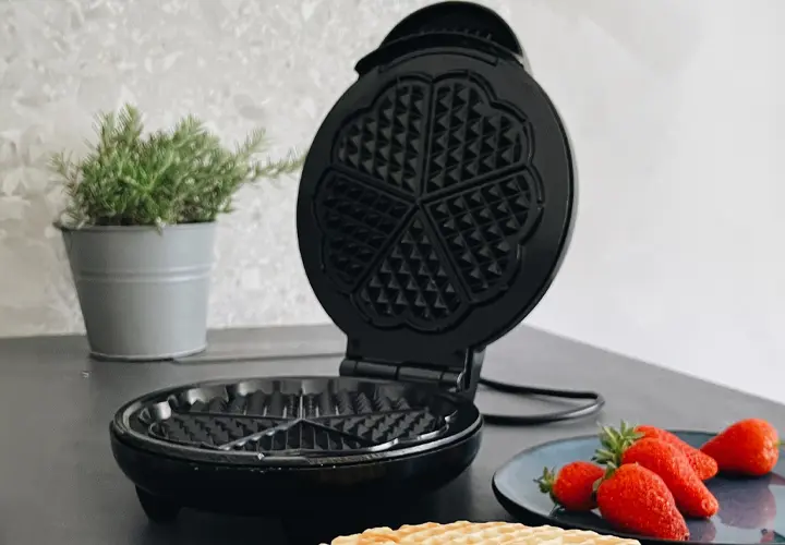Ein Waffeleisen mit leckeren Waffeln und Erdbeeren.