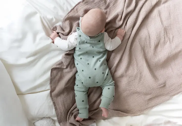 Ein Baby in einem grünen Sternenkostüm liegt auf einer weichen, strukturierten Decke und ruht friedlich in einem weißen Bett. Ein Baby in einem grünen Sternenkostüm liegt auf einer weichen, strukturierten Decke und ruht friedlich in einem weißen Bett.