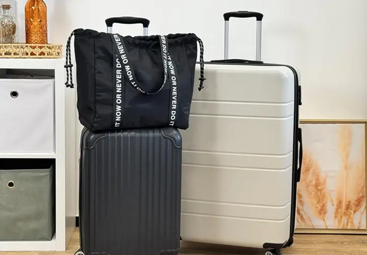 Eine schwarze Tasche mit Kordelzug sitzt auf einem schwarz-silbernen Koffer, der neben einem weißen Koffer in einem stilvollen Reise-Setup angeordnet ist.