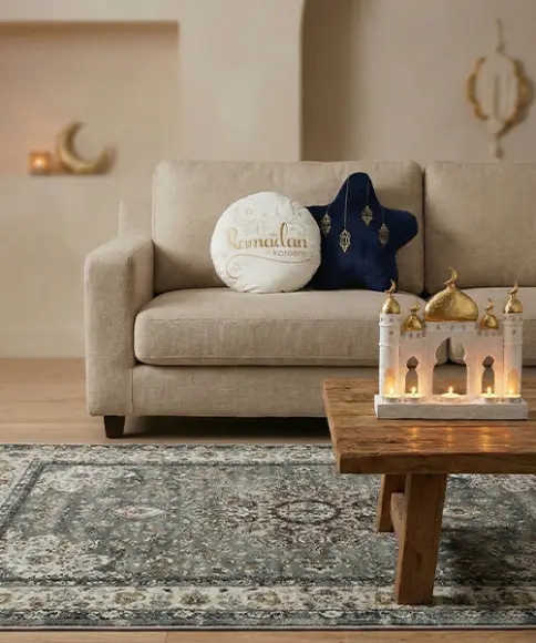 Ein gemütliches Wohnzimmer mit einem beigen Sofa mit dekorativen Kissen, einem Holztisch und einem kerzenhalter in Form einer Moschee.