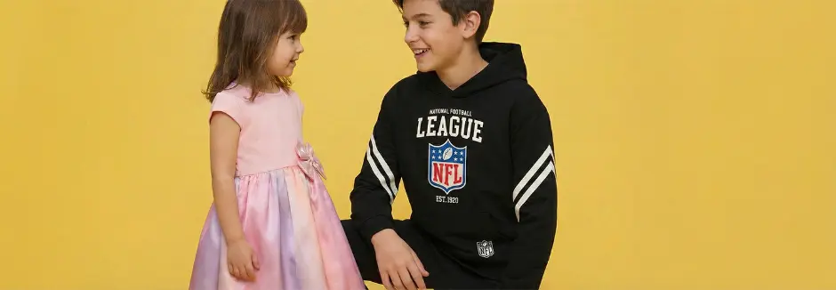 Ein junges Mädchen in einem pinken Kleid steht neben einem Jungen in einem schwarzen NFL-Hoodie vor einem leuchtend gelben Hintergrund.