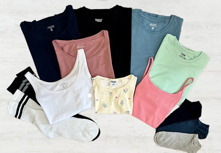 Ein Flatlay aus verschiedenen bunten Tops und Socken, darunter Tanktops und T-Shirts in Blau-, Pink-, Grün-, Weiß- und Gelbtönen.