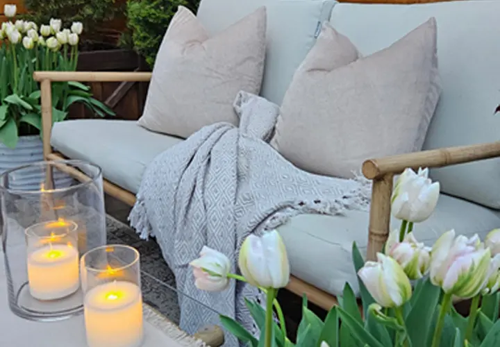 Gemütliche Sitzgelegenheit im Freien mit weichen Kissen, einer Kuscheldecke, Kerzen und blühenden Tulpen