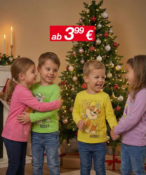 Drei Kinder in bunten T-Shirts stehen neben einem geschmückten Weihnachtsbaum, im Hintergrund sind Kerzen zu sehen und über ihnen hängt ein Preisschild.