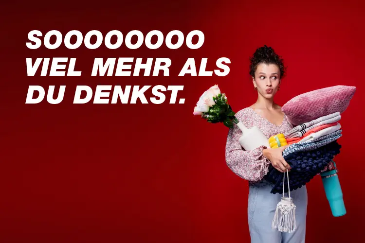 Eine Person hält mehrere bunte Gegenstände, darunter Decken, eine Wasserflasche und Blumen, vor einem leuchtend roten Hintergrund.