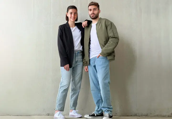 Ein Mann und eine Frau stehen Seite an Seite vor einer schlichten Wand, beide tragen Freizeitkleidung mit Jeans und Turnschuhen.