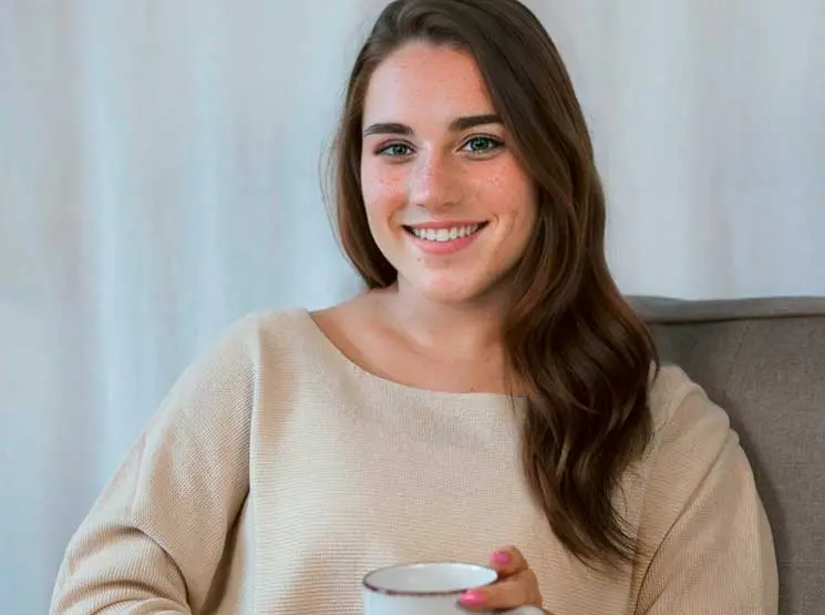 Eine Frau sitzt auf einem Sofa und hält eine Tasse Kaffee in der Hand.