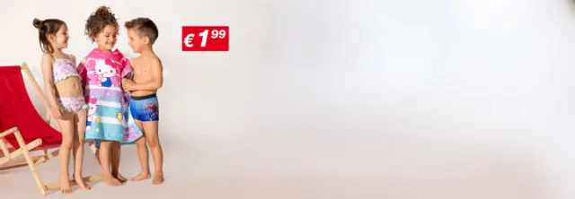 Drei Kinder in Badekleidung stehen zusammen, eines davon in ein buntes Hello Kitty-Handtuch gewickelt, im Hintergrund ein Strandstuhl und ein Strohsonnenschirm.