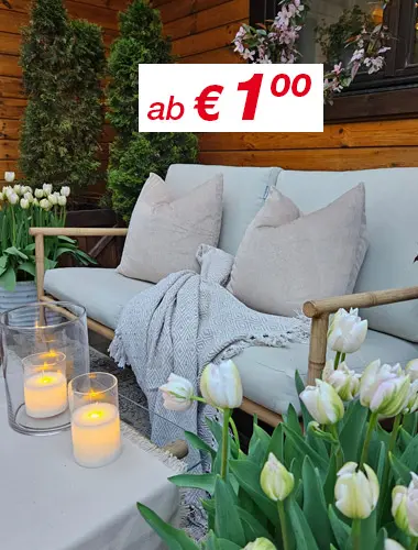 Gemütliche Sitzgelegenheiten im Freien mit weichen Kissen, einer gestrickten Decke, leuchtenden Kerzen und blühenden Tulpen vor einem Holzhintergrund.