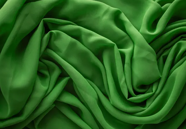 Eine Nahaufnahme von luxuriösem grünem Stoff, elegant drapiert und geknittert, der seine glatte Textur und lebendige Farbe zur Geltung bringt.