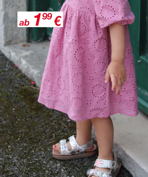 Ein kleines Kind steht draußen in einem rosa Kleid mit ausgestanztem Blumenmuster. Ein Teil des Fußes ist in stylischen Sandalen zu sehen. Preisschild sichtbar.