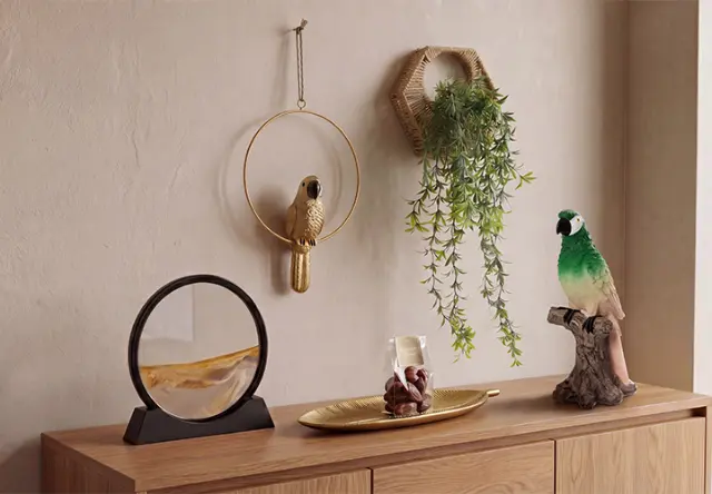 Dekorative Wohnaccessoires mit Papageienfiguren, Wanddeko und Hängepflanze auf einer Holzkommode im Dschungel-Look