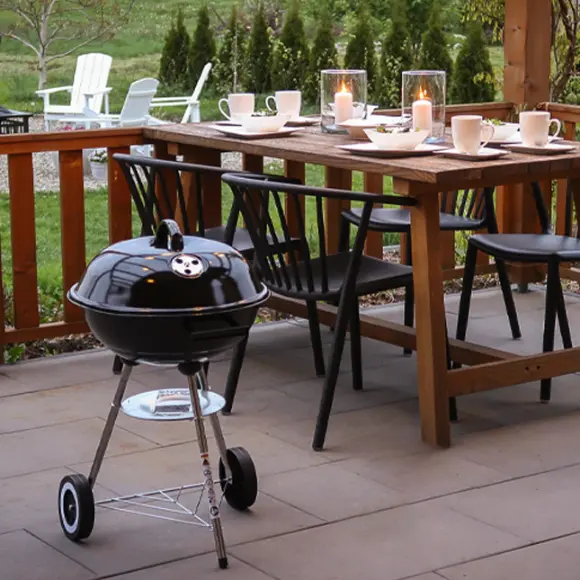 Ein gemütlicher Essbereich im Freien mit einem Holztisch mit Kerzen, Stühlen und einem kleinen schwarzen Grill daneben, inmitten eines grünen Gartens.