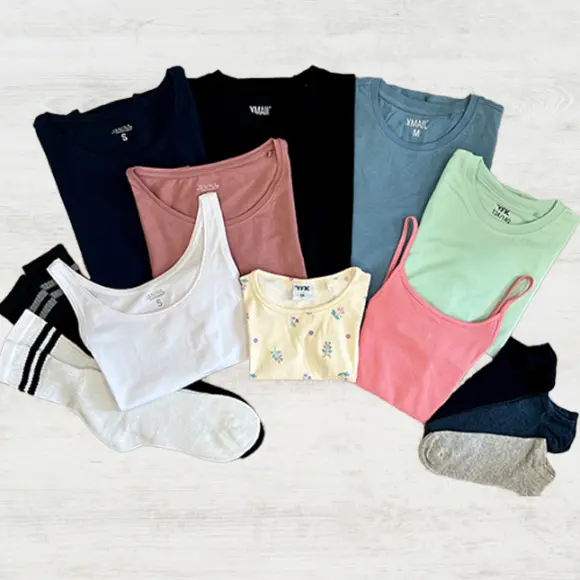Ein Flatlay aus verschiedenen bunten Tops und Socken, darunter Tanktops und T-Shirts in Blau-, Pink-, Grün-, Weiß- und Gelbtönen.
