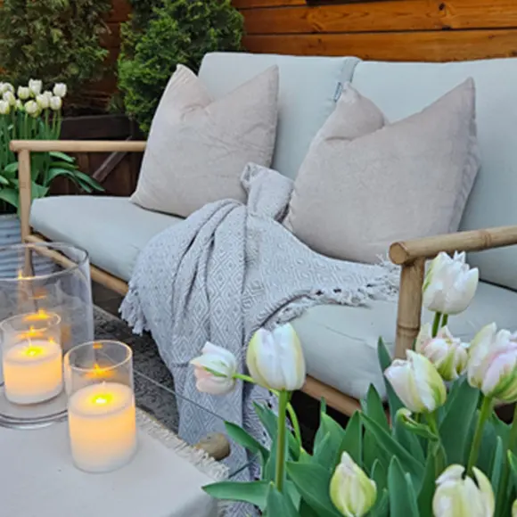 Gemütliche Sitzgelegenheit im Freien mit weichen Kissen, einer Kuscheldecke, Kerzen und blühenden Tulpen