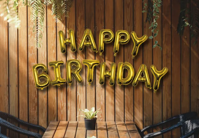 Goldene Luftballons mit dem Spruch „Happy Birthday“ an einer Holzwand