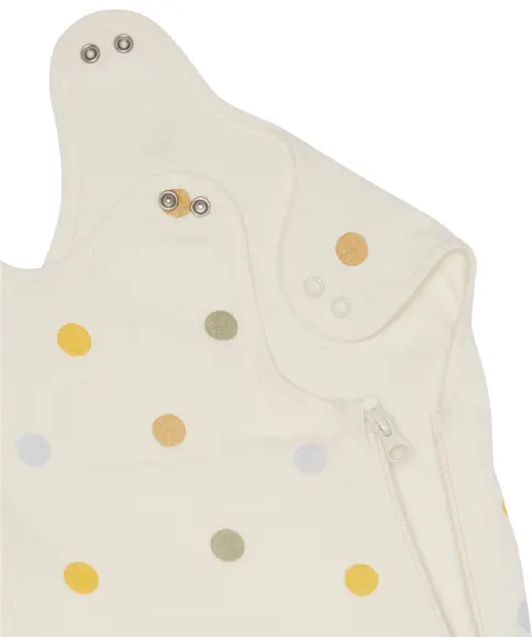 Nahaufnahme eines cremefarbenen Baby-Schlafsacks mit senfgelben, hellbraunen, hellblauen, olivegrünen Punkten, Druckknöpfen und einem seitlichen Reißverschluss.