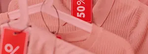 Nahaufnahme von rosa Kleidung mit roten „50 %“-Rabatt-Schildern an weißen Bügeln.