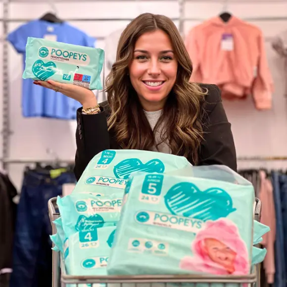 Eine Person hält eine Packung Poopeys-Feuchttücher, umgeben von gestapelten Packungen