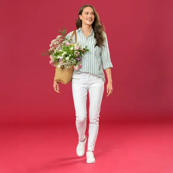Eine Person in einem gestreiften Hemd und einer weißen Hose hält einen Korb mit bunten Blumen in der Hand.