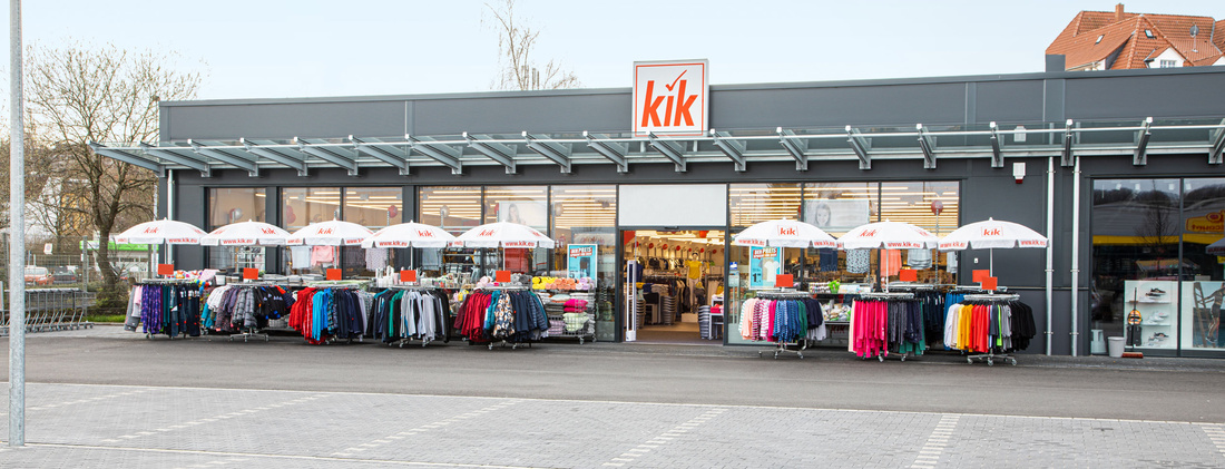Außenansicht einer KiK-Filiale mit KiK-Logo auf der Tür und Kleiderständern vor dem Eingang