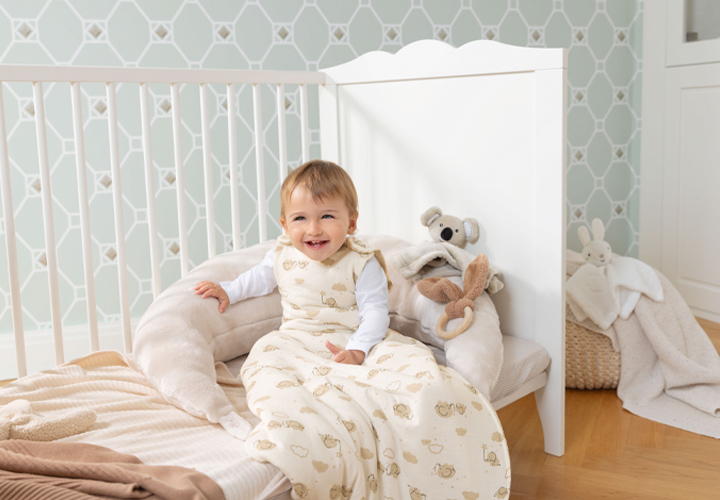 Ein Kleinkind in einem kuscheligen Schlafsack sitzt bequem in einem Kinderzimmer mit Plüschtieren.