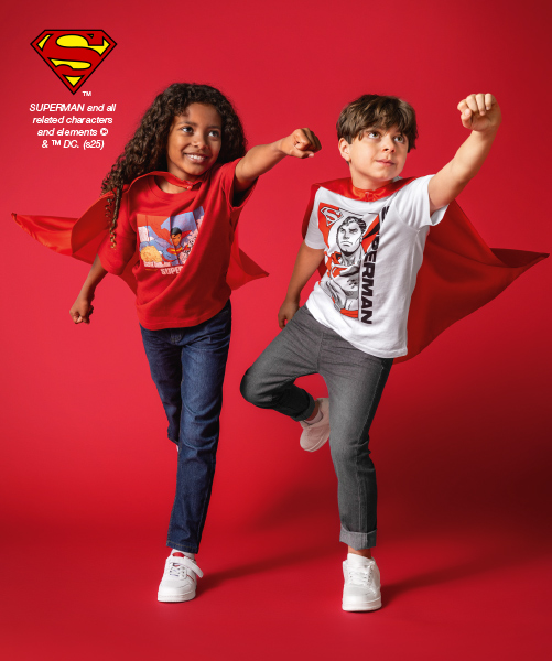 Zwei Kinder in Superheldenumhängen posieren selbstbewusst vor rotem Hintergrund und zeigen spaßige Superman-Outfits.