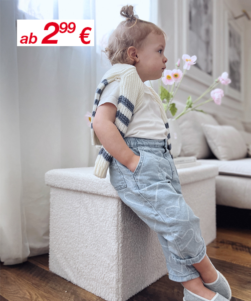 Ein Kind lehnt an einem weißen Hocker, trägt einen gestreiften Pullover und eine hellblaue Hose, im Hintergrund ein modernes Wohnzimmer mit frischen Blumen.